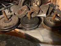 Photo of various weight plates stacked on two metal rods, showing wear and rust, with some plates labeled 25 lbs.