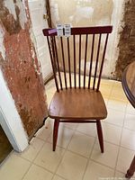 Front view of a wooden chair with spindle back, showing the seat and legs with reddish-brown finish and scratches.