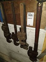 Six pipe wrenches hanging on a wooden board, showing wear and rust.