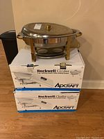 Two boxed rectangular Rockwell chafing dishes stacked with one constructed chafing dish on top, showcasing original packaging boxes.