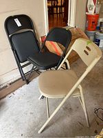 Three folding chairs: two black padded and one beige padded with visible signs of wear and scratches.