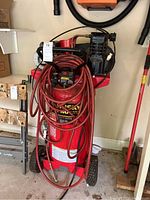 Front view of red vertical compressor with coiled hose