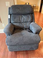 Front view of the gray fabric La-Z-Boy electric recliner chair showing cushioned backrest, armrest, and remote control on seat.