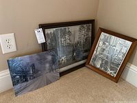 Three items displayed together angled in corner: two framed art pieces depicting 1800s logging scenes and one metal art piece of the Fox Theater.