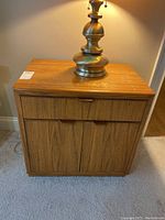 Front view of one Drexel nightstand with brass lamp on top, showing drawer and cabinet doors.