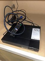 Sony BDP-S3700 Blu-Ray player shown on shelf with remote and cables on top.