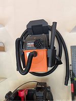 Ridgid Stor N Go wet/dry vacuum with hose and accessories visibly attached, mounted on wall storage shelf.