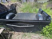 Side view of black BODYGARD truck bed liner showing ribbed texture and molded wheel wells, outdoors in grass.