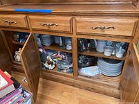 Open wooden cabinet showing multiple shelves with stacked fine china, tea sets, and figurines inside.