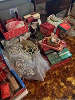 Overview photo showing many Christmas decorations including string lights, boxes of ornaments, faux greenery, and holiday figurines on a carpeted floor.