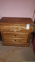 Photo showing the front of one oak nightstand, two drawers with carved detailing and round metal pulls.