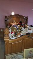 Full view of carved oak bed filled with stuffed animals, showing headboard and footboard wood details