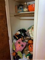 Closet shelf with various Halloween-themed decorations including a pink metal owl yard decor, assorted small figurines, and plastic pumpkin containers.