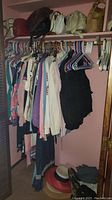Full view of closet showing clothing on hangers below the handbags and hats on the floor.