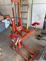 Front view of orange Hein Werner flat lift showing adjustable lifting arms with red padded ends, hydraulic pump, and wheels.