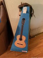 Hohner branded blue box for a classical guitar held upright with some guitar straps draped on top.
