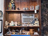 Full view of three wooden shelves with assorted ceramic and stone animal figurines, a basket, and decorative objects including a dog figurine, mirror, and owl planter.