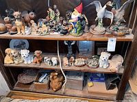 Shelf with a large variety of animal figurines including bears, cats, dogs, ducks, and a garden gnome, mostly wooden and ceramic, various colors and styles.