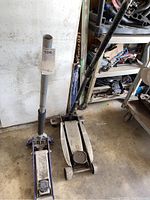Two hydraulic floor jacks side by side, one purple framed and one plain metal.