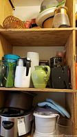 Shelf showing crock pot, green pitcher, glass and plastic vases, black and white kitchen appliance
