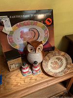 Photo showing the Nasco Earthenware Turkey Platter box, ceramic owl cookie jar, measuring cups set in box with owl design, salt and pepper shakers, and a turkey-design decorative bowl on a wooden surface.