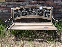 Front view of weathered outdoor settee bench showing metal grapevine design on backrest and wooden slat seat.