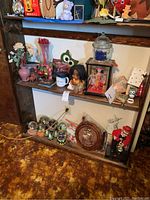 Overview of wooden brown shelves displaying various collectibles including snow globes, owl-themed art, dolls, music box, and holiday decorations.
