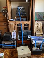 Wide view showing a collection of vintage and modern electronics including stereo components stacked on a wooden cabinet, toasters, boxed electronics, and portable turntable case.