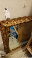 Full view of the ornate gold framed mirror leaning against a wall on the floor.