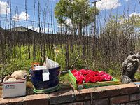Outdoor shot showing large blue ceramic planter with metal flower and orange owl garden stake on a brick ledge, with a concrete or stone owl statue nearby.