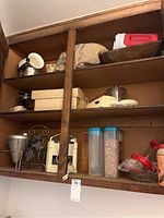 Wooden shelves filled with kitchen items, including plastic containers, metal strainer, glass jars, and a metal wine rack.