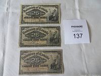 Three 25 cent shinplasters from 1900 displayed flat on white cloth background with Maxsold lot number card.