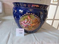 Wide angle photo of the full jardiniere showing blue and gold decoration with one English romantic scene visible.