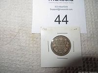 Photo of the obverse side of the 1910 Canadian 25 cent silver coin housed in a white cardboard holder with staple corners.