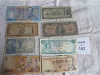Collection of eight different banknotes from various countries laid out on a white fabric background.