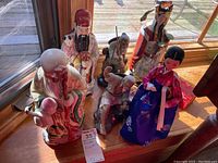 Six Asian figurines including elderly men in traditional attire and a female doll in traditional Korean hanbok, displayed on wooden surface.