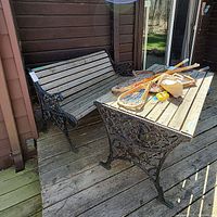 Metal and wood slatted bench and table on wooden deck, showing weathered finish and decorative metal sides. Items are heavy and suitable for outdoor use.