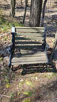 Front view of sturdy outdoor bench with weathered wooden seat and backrest slats and decorative black metal sides.
