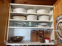 White ribbed CorningWare casserole baking dishes and glass bowls stacked on shelves, wooden canisters and jar on bottom shelf