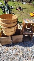 Wooden crates and round wooden fruit baskets outdoors on gravel and grass, golf equipment and lawn mowers visible in background.