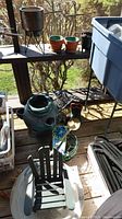 Overview of garden items on a porch including the Adirondack style chair, ceramic birdhouse, terracotta planters, metal tools, black plastic pots, and some wooden items