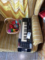 Casio SK-1 keyboard resting on original box on striped chair with basket of maracas beside it