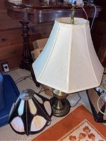 Full view showing the table lamp with the cream fabric shade and brass-tone base alongside the stained glass style shade on the floor.
