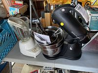 Photo showing the white Proctor Silex blender with a clear glass jar next to the black Sunbeam Mixmaster stand mixer with two stacked stainless steel bowls holding multiple metal beaters.