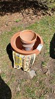 Top view of stack of five terracotta clay pots and saucer on outdoor grass with sunlight. Newspaper visible around base.
