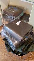 Stack of folded grey tarps still in original plastic packaging with barcode visible, placed on shelf and in box below with camouflage tarp.