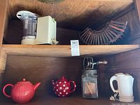 Shelf with Braun food processor, vintage fan, two red teapots, and glass jar churn.