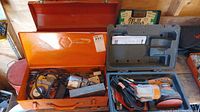 Orange metal tool box containing an older model corded power drill, various tools, and accessories.