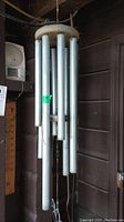Full view of a weathered metal wind chime with multiple silver tubes hanging from a wooden circular top.