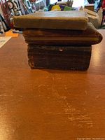 Three small antique books stacked on a wooden surface showing worn covers and bindings.